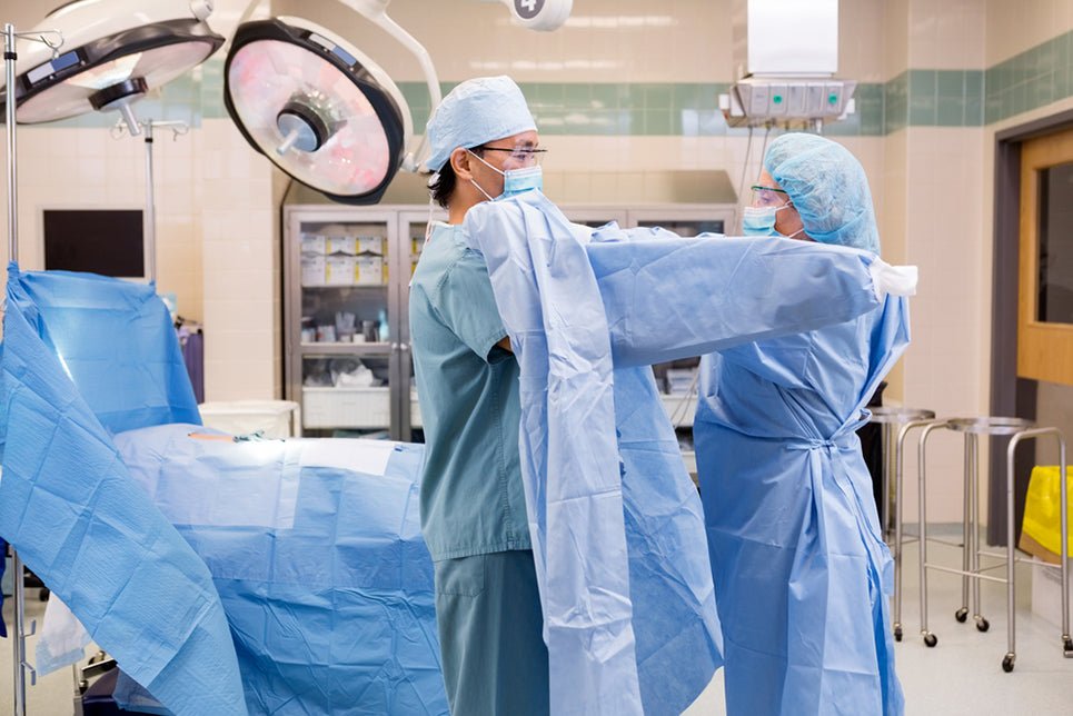 Side view of mature scrub nurse assisting surgeon putting on sterile operating gown