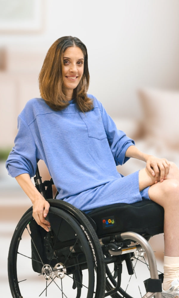 Woman in a wheelchair wearing a light blue top and shorts indoors.