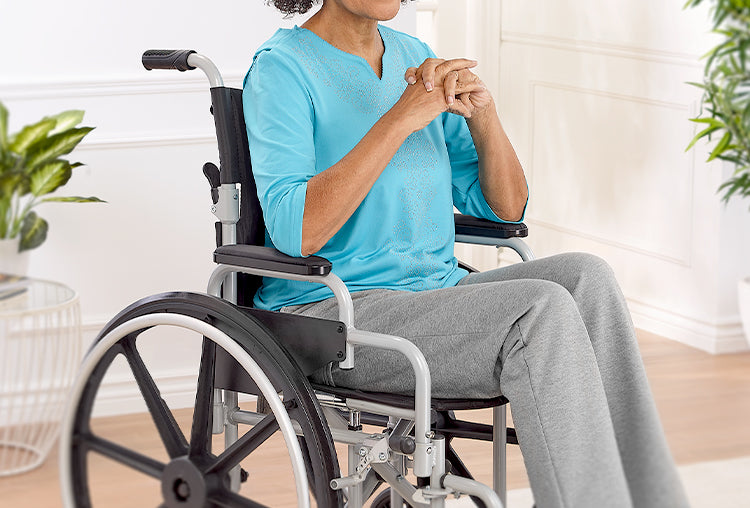 Person seated in a wheelchair wearing a blue adaptive top and gray pants in a bright indoor setting.
