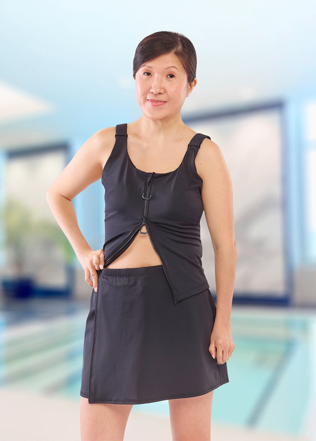 Woman wearing a black tank top and skirt standing by a pool.