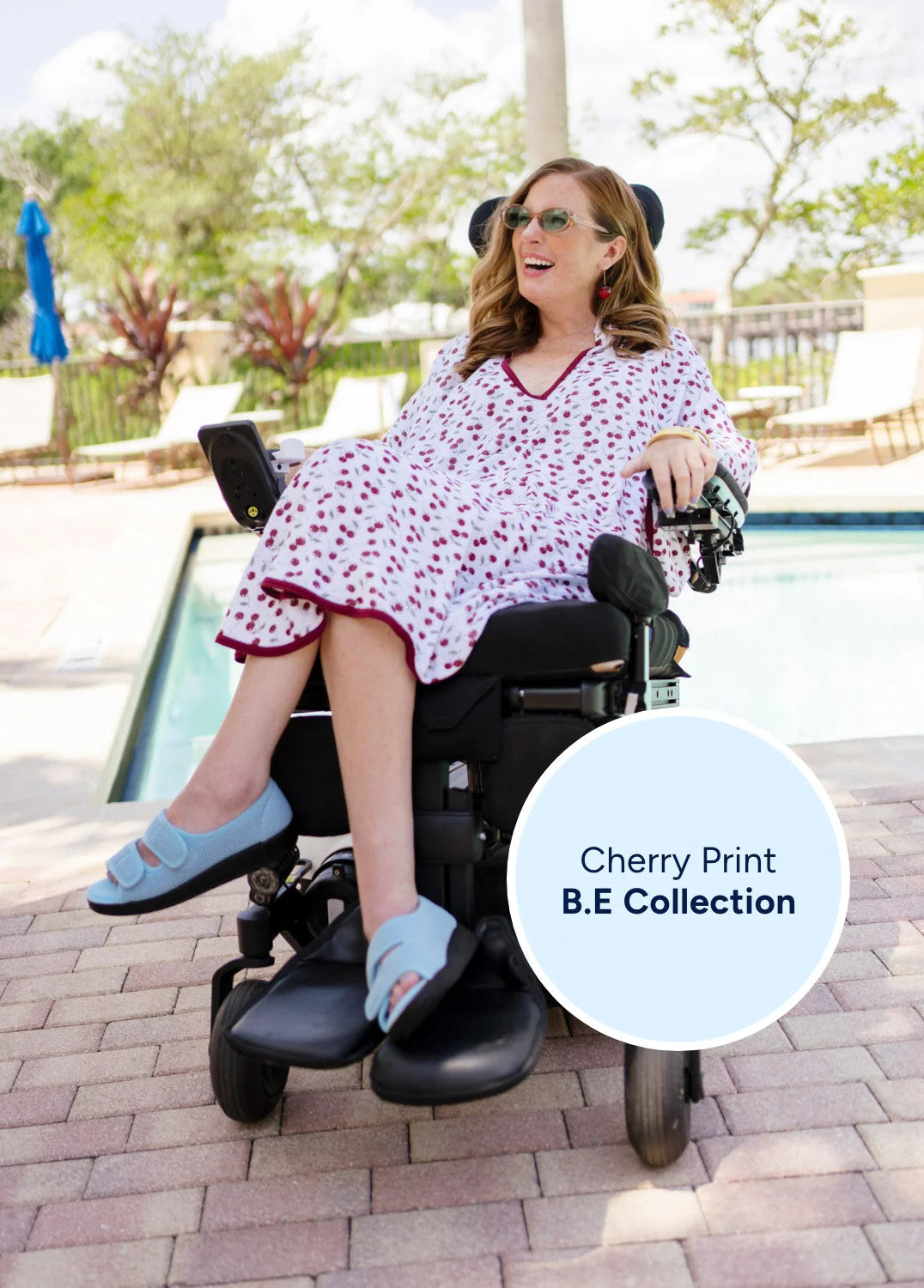 Woman in a wheelchair wearing a cherry print dress by a poolside.